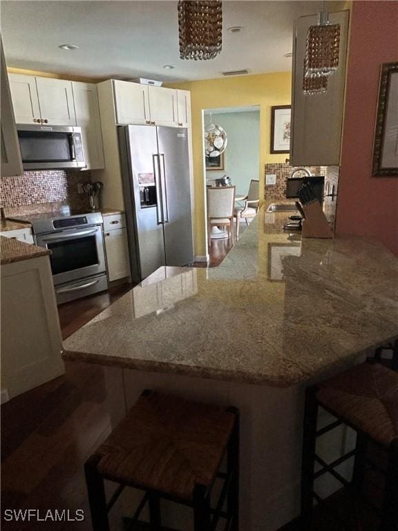 kitchen with white cabinetry, light stone counters, appliances with stainless steel finishes, a kitchen breakfast bar, and decorative backsplash