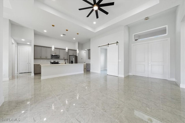 unfurnished living room with a high ceiling, a raised ceiling, a barn door, and ceiling fan