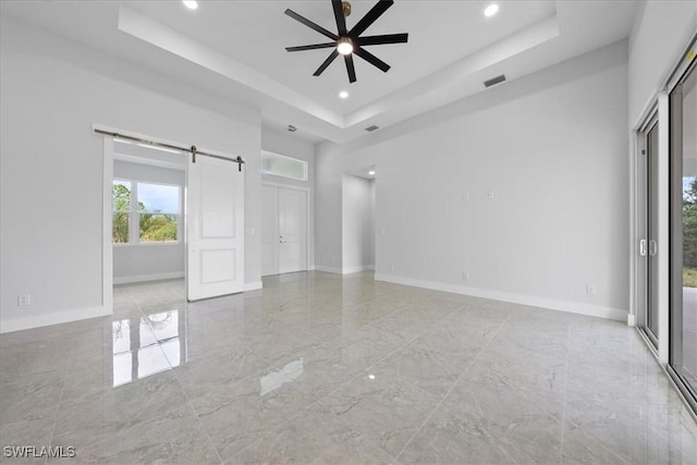 spare room featuring a barn door, ceiling fan, a tray ceiling, and a high ceiling