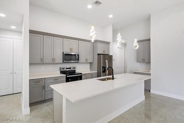 kitchen with appliances with stainless steel finishes, gray cabinetry, a center island with sink, and pendant lighting