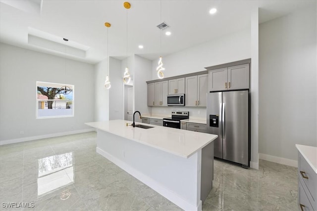kitchen with pendant lighting, sink, gray cabinets, appliances with stainless steel finishes, and a center island with sink