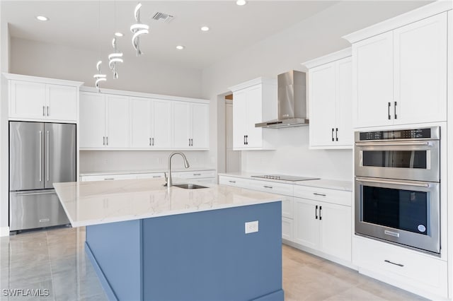 kitchen with appliances with stainless steel finishes, sink, wall chimney range hood, and a center island with sink