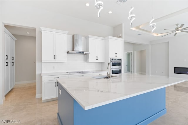 kitchen with white cabinets, wall chimney exhaust hood, and a large island