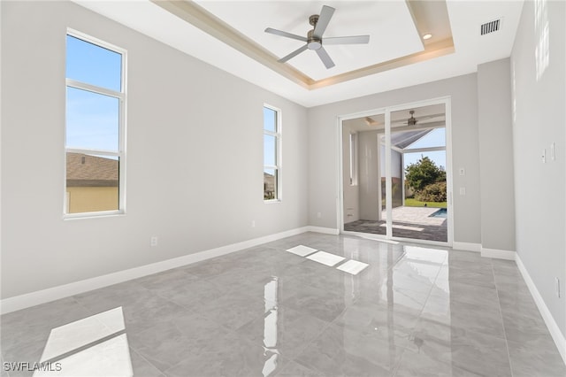 spare room with ceiling fan, a raised ceiling, and a healthy amount of sunlight