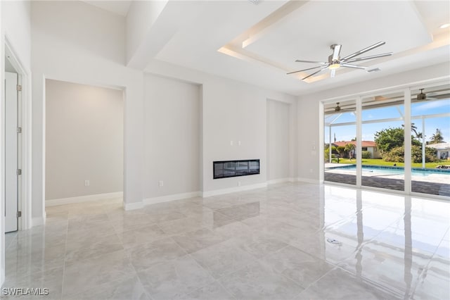 unfurnished living room with ceiling fan and a raised ceiling