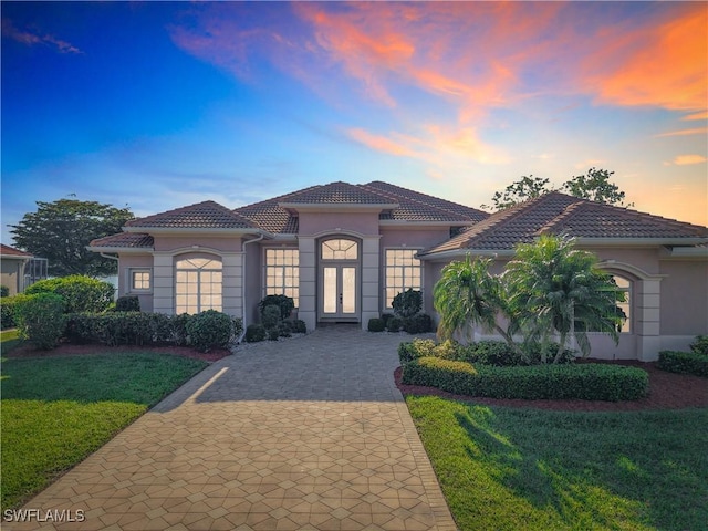 mediterranean / spanish home with a tiled roof, a yard, decorative driveway, french doors, and stucco siding