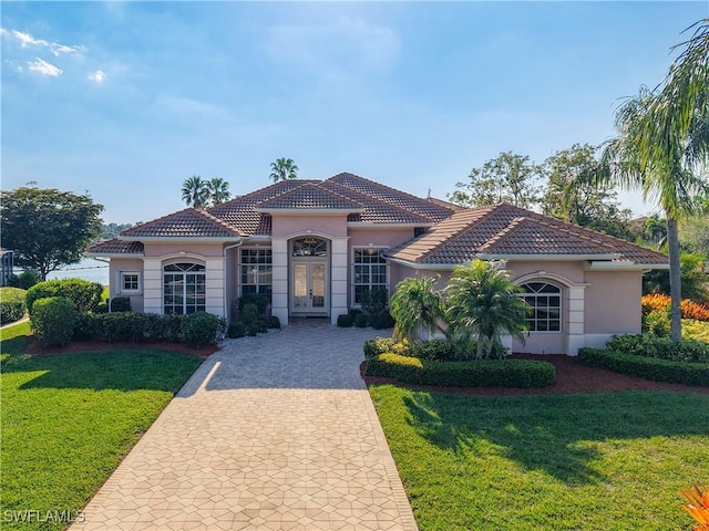 mediterranean / spanish home with a tiled roof, decorative driveway, french doors, a front yard, and stucco siding