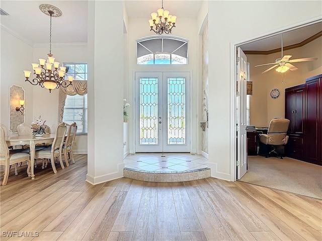 entryway featuring an inviting chandelier, crown molding, light wood-style floors, and french doors