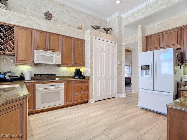 kitchen with white appliances, light wood-style flooring, dark stone countertops, crown molding, and a sink