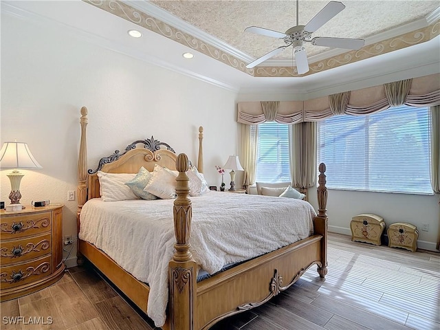 bedroom with ornamental molding, a tray ceiling, baseboards, and wood finished floors