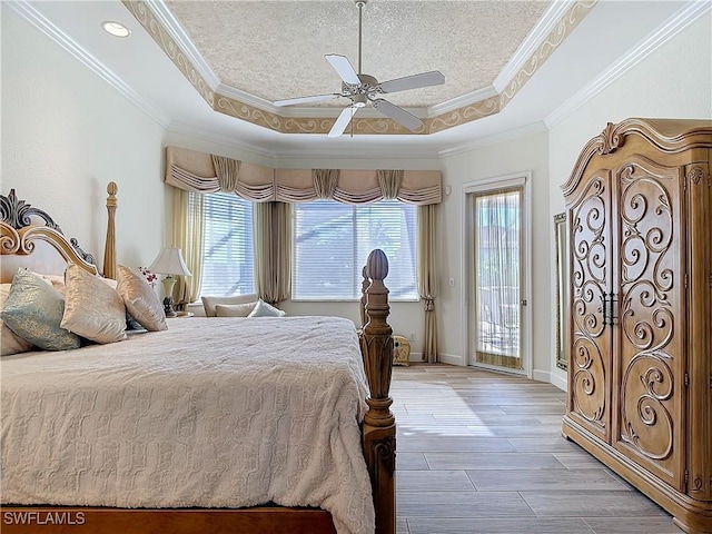 bedroom featuring a tray ceiling, multiple windows, light wood-style flooring, and access to exterior