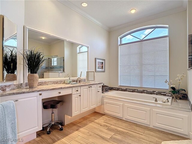 bathroom featuring a garden tub, crown molding, wood finished floors, and vanity