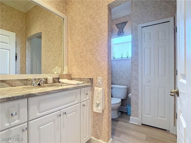 bathroom with a closet, vanity, toilet, and wallpapered walls