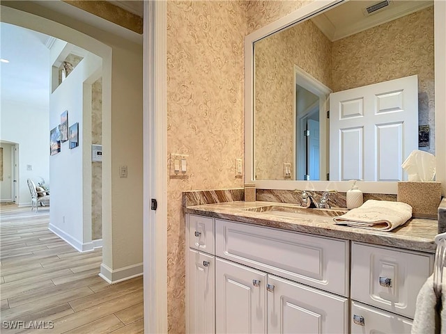 bathroom featuring wood finish floors, visible vents, vanity, baseboards, and wallpapered walls