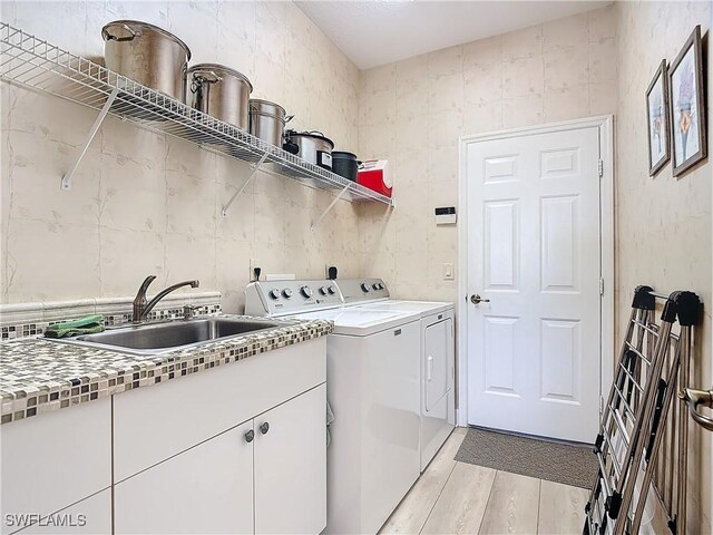 laundry room featuring light wood-style flooring, washer and clothes dryer, a sink, and cabinet space