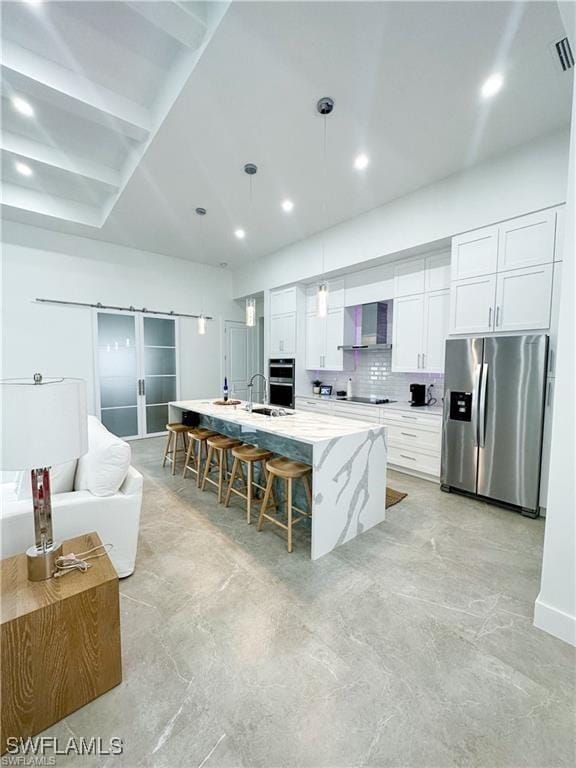 kitchen with stainless steel refrigerator with ice dispenser, white cabinetry, an island with sink, and hanging light fixtures