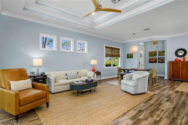 living room with wood finished floors, a ceiling fan, baseboards, ornamental molding, and a tray ceiling