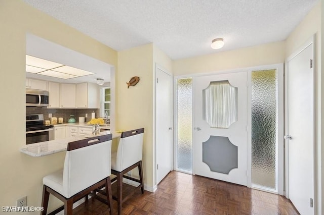 2228 Poinciana Dr, Naples, FL 34105 - kitchen with backsplash, a kitchen bar, a textured ceiling, a peninsula, and stainless steel appliances