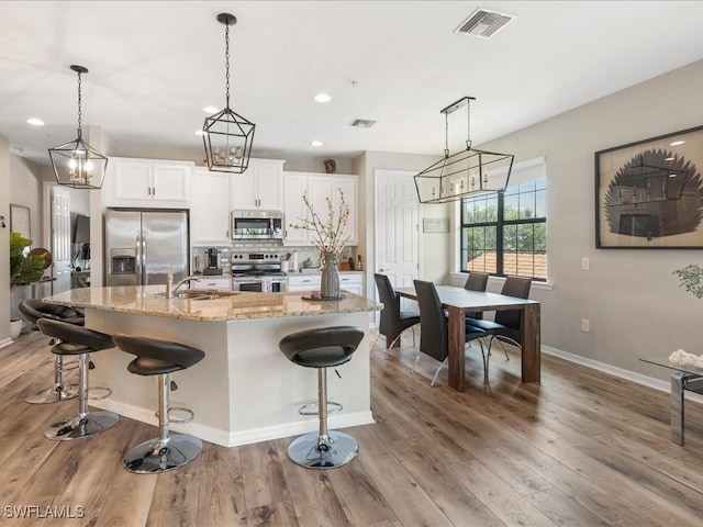 kitchen featuring visible vents, light wood-style flooring, appliances with stainless steel finishes, white cabinets, and a sink