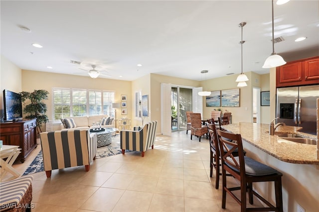 kitchen with stainless steel fridge, light stone counters, a breakfast bar, hanging light fixtures, and a sink