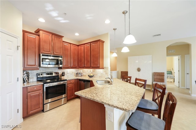 kitchen with arched walkways, stainless steel appliances, a peninsula, a sink, and decorative light fixtures
