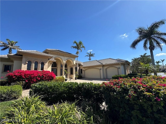 mediterranean / spanish-style home with an attached garage, a tile roof, and stucco siding