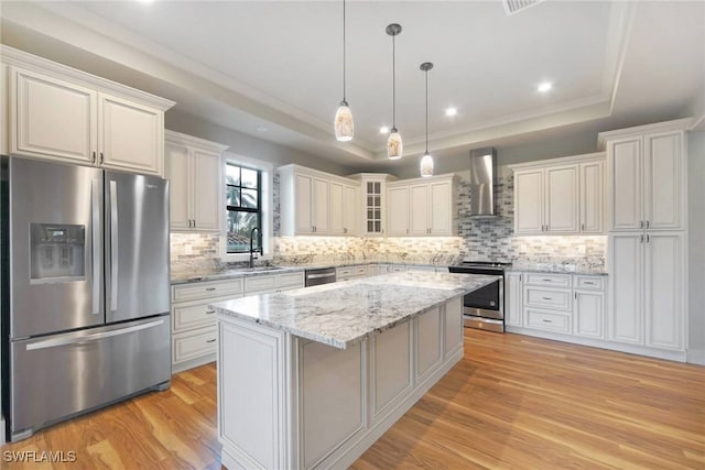 kitchen featuring a tray ceiling, appliances with stainless steel finishes, wall chimney range hood, and glass insert cabinets