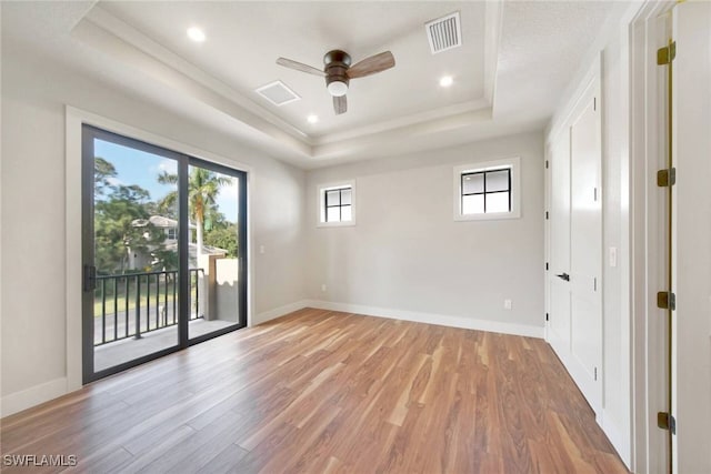 empty room featuring a tray ceiling, light wood finished floors, visible vents, a ceiling fan, and baseboards