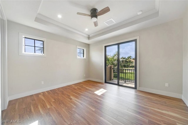 empty room with a tray ceiling, visible vents, light wood-style floors, a ceiling fan, and baseboards