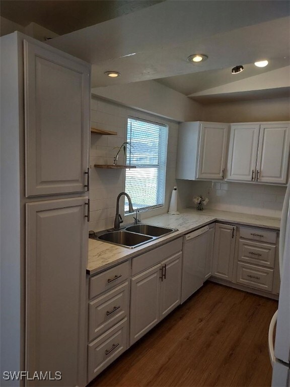 kitchen with sink, white dishwasher, white cabinets, dark hardwood / wood-style flooring, and decorative backsplash