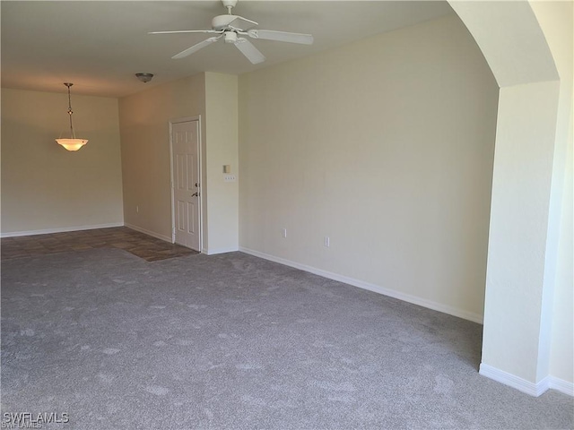 carpeted empty room with ceiling fan, baseboards, and arched walkways