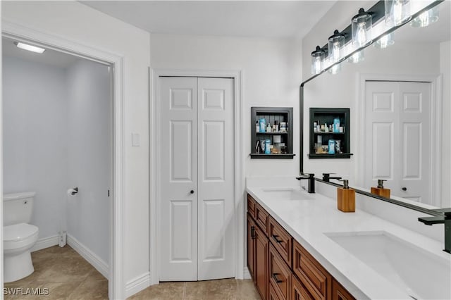 bathroom with a closet, a sink, toilet, and double vanity