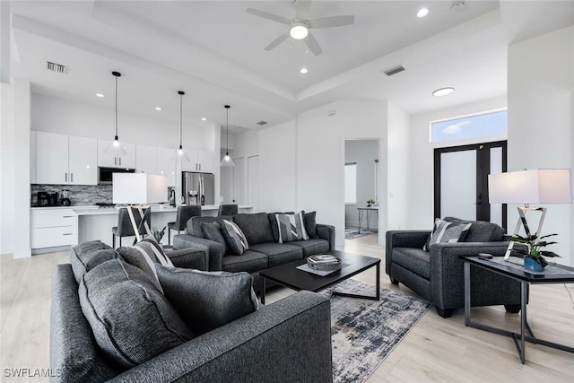 living room with ceiling fan, a towering ceiling, a raised ceiling, and light hardwood / wood-style flooring