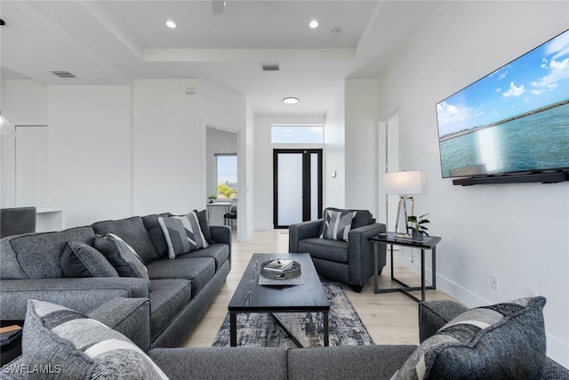 living room featuring a raised ceiling, light hardwood / wood-style floors, and a high ceiling