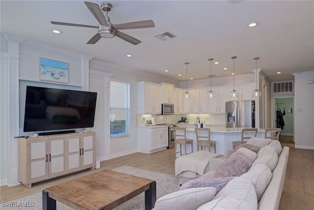 living area featuring light wood-style floors, recessed lighting, visible vents, and crown molding