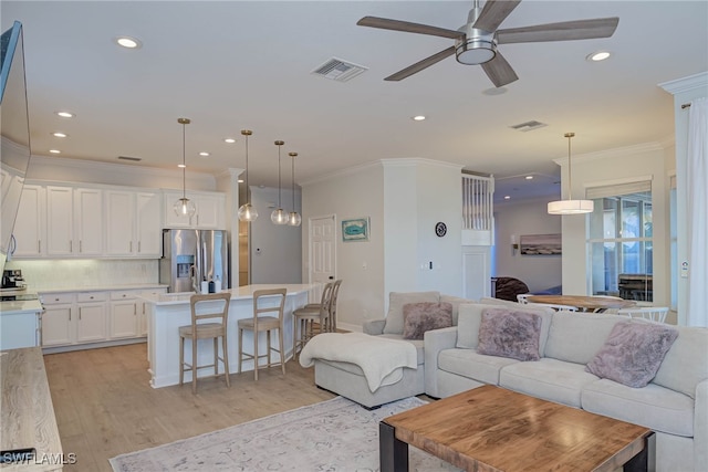 living room featuring light wood-type flooring, visible vents, crown molding, and recessed lighting