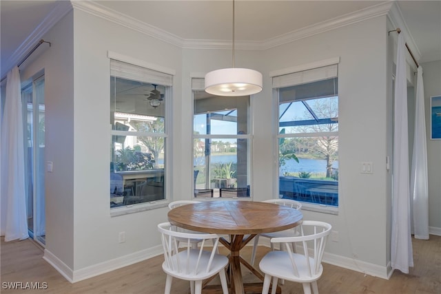 dining space featuring a water view, light wood finished floors, and crown molding