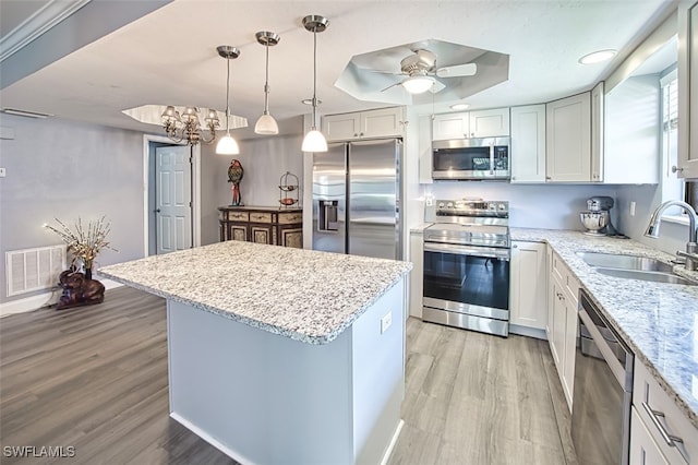 kitchen with sink, decorative light fixtures, a tray ceiling, stainless steel appliances, and white cabinets