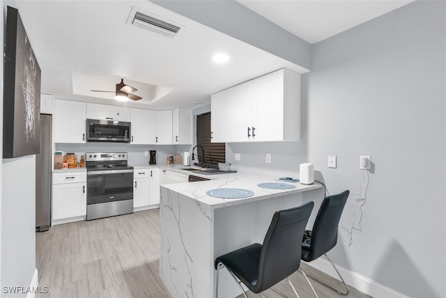 kitchen featuring white cabinetry, light stone counters, appliances with stainless steel finishes, a tray ceiling, and kitchen peninsula