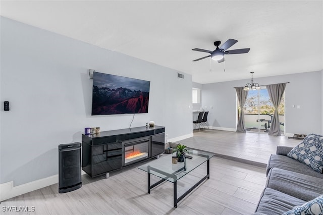 living room with ceiling fan with notable chandelier and light hardwood / wood-style floors