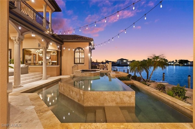 pool at dusk with an in ground hot tub, a water view, and a patio area