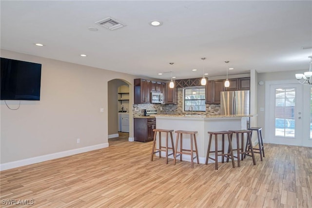 kitchen with visible vents, backsplash, light wood-type flooring, arched walkways, and stainless steel appliances