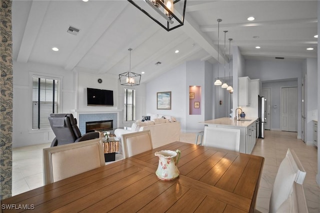 dining space with light tile patterned floors, a chandelier, visible vents, beamed ceiling, and a glass covered fireplace