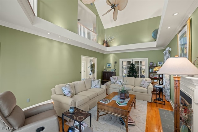 living room with a high ceiling, ceiling fan, ornamental molding, and light wood-type flooring