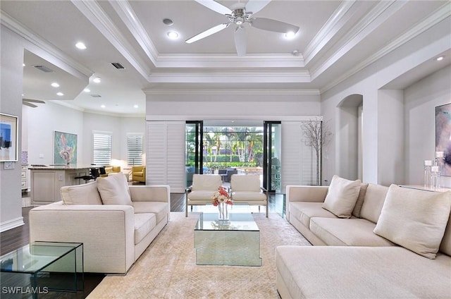 living room with ceiling fan, ornamental molding, a tray ceiling, and light hardwood / wood-style floors