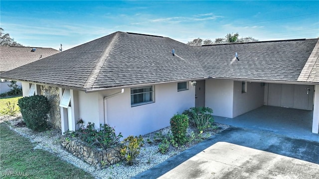 view of home's exterior with a carport, stucco siding, concrete driveway, and roof with shingles