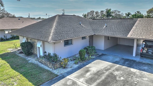 view of side of home featuring driveway, stucco siding, an attached carport, and roof with shingles