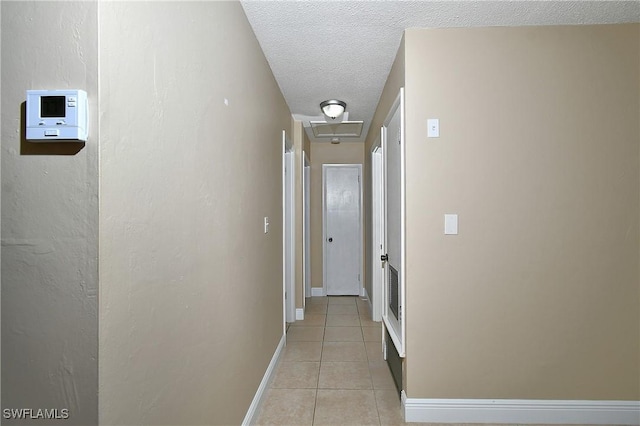 hallway with light tile patterned floors, attic access, baseboards, and a textured ceiling