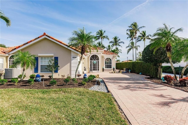 mediterranean / spanish home with stucco siding, a tiled roof, decorative driveway, and a front lawn