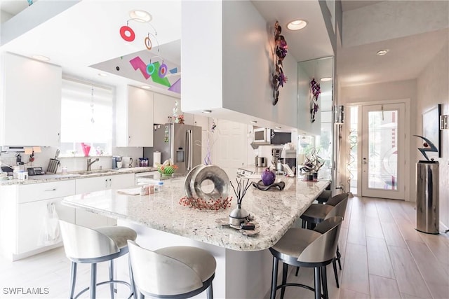 kitchen with white cabinetry, light stone countertops, a kitchen breakfast bar, and stainless steel refrigerator with ice dispenser